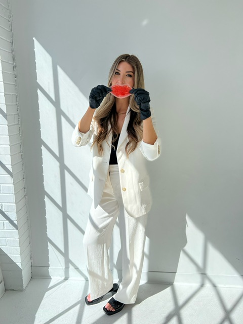 A person in a white suit and black gloves holds a red object against a bright, sunlit background.