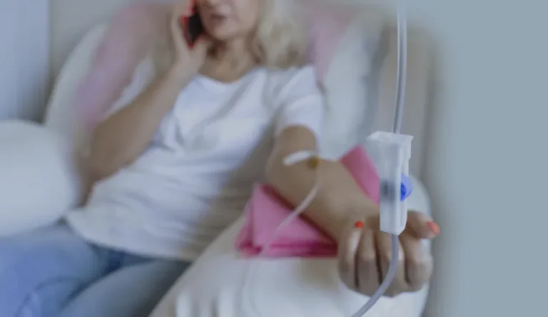 A person sits on a couch, receiving an IV infusion, while talking on a phone at Point of View Medical Aesthetics
