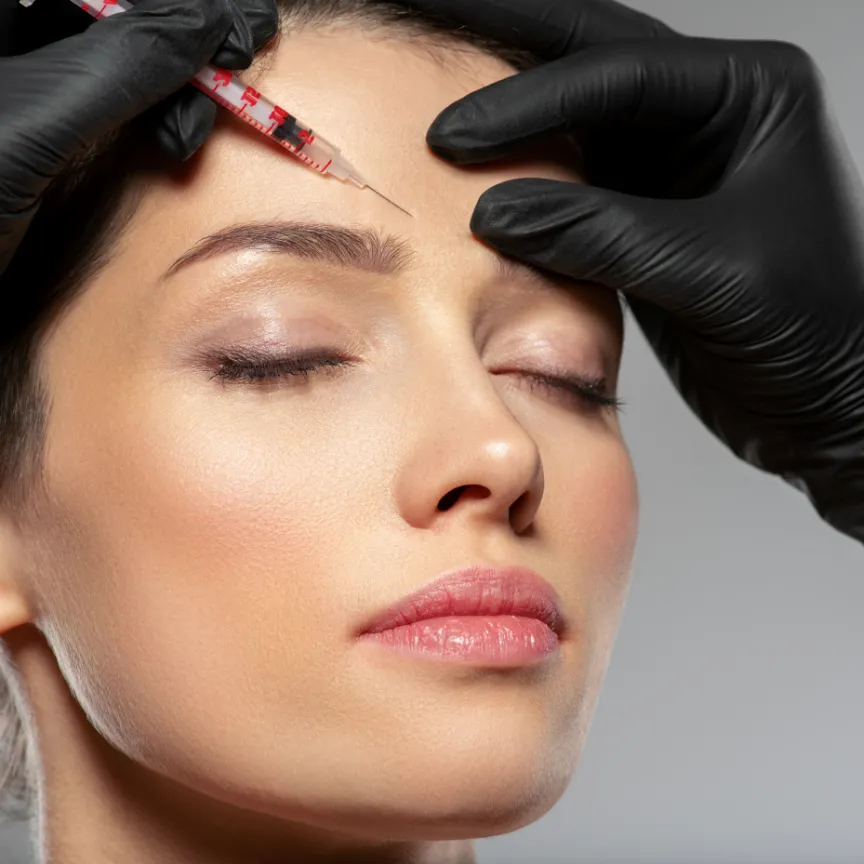 A woman receives a forehead injection from a gloved professional.