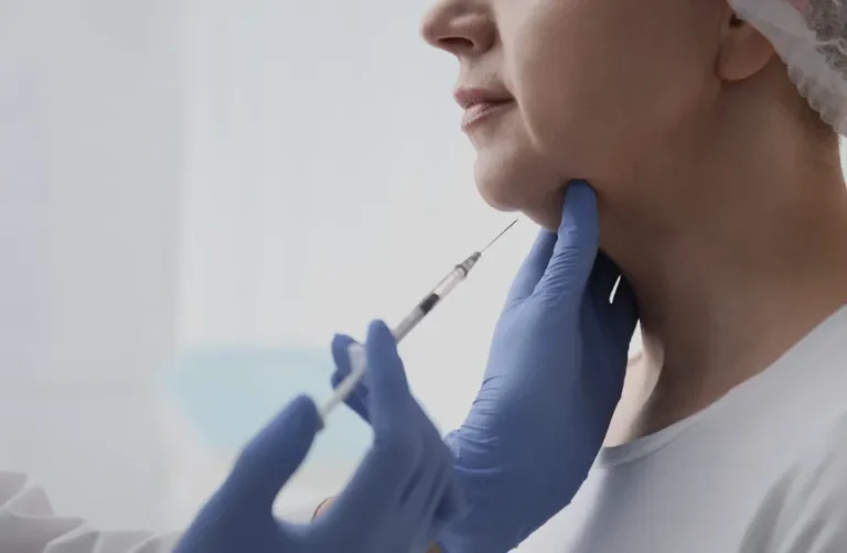 A person receives a cosmetic injection for dissolving fat in the chin area from a gloved professional.